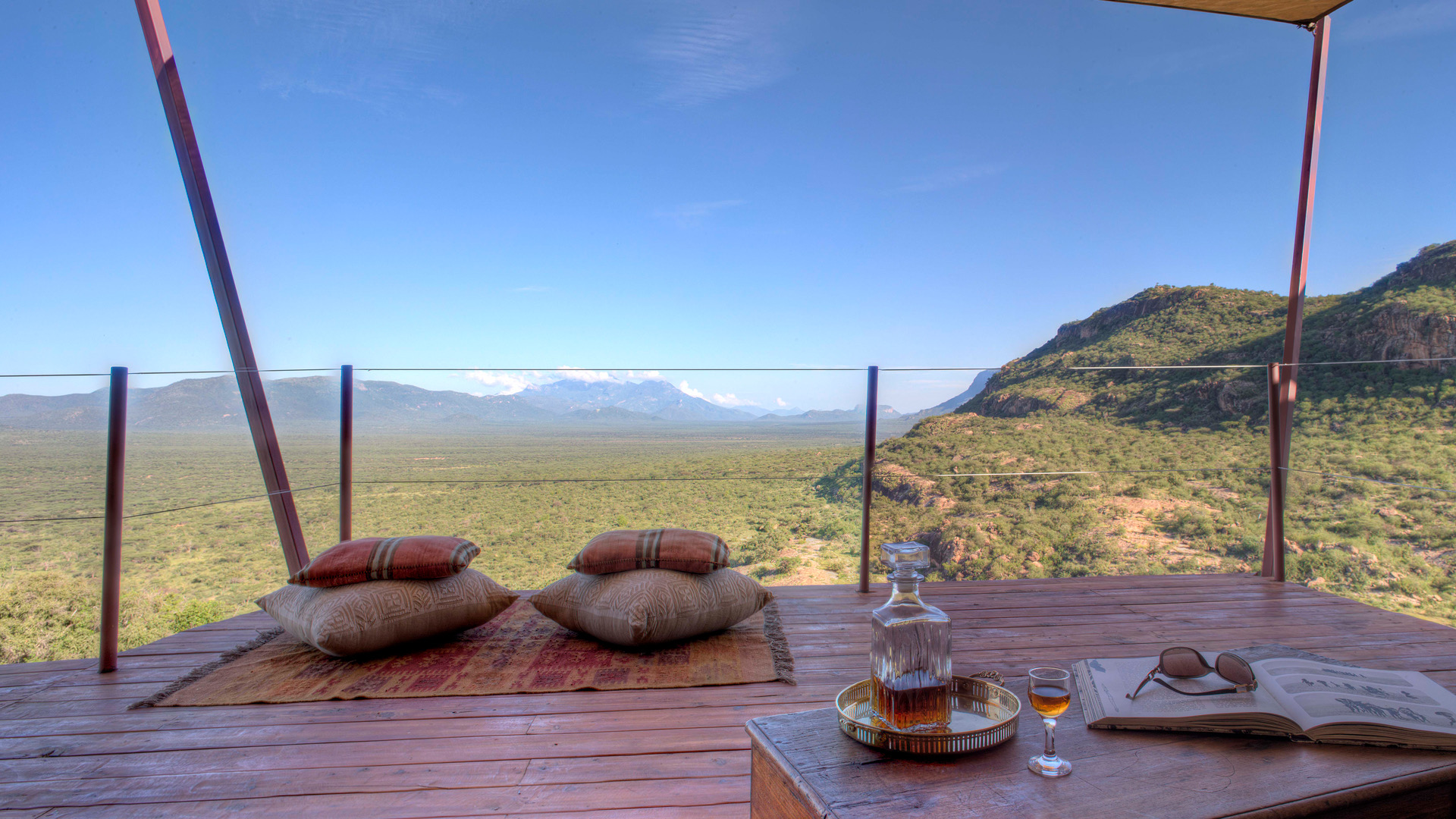 A deck with floor cushions and a low table, looking out over the plains